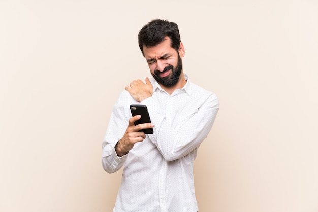 Young man with beard holding a mobile suffering from pain in shoulder for having made an effort