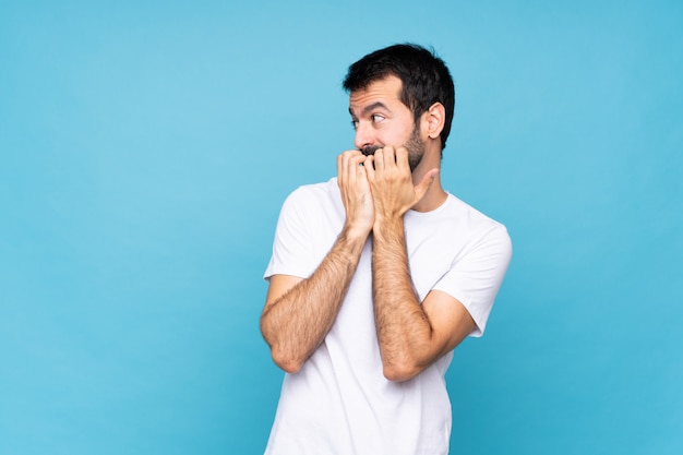 Young man with beard  over isolated blue  nervous and scared putting hands to mouth