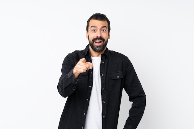 Young man with beard over isolated white background surprised and pointing front