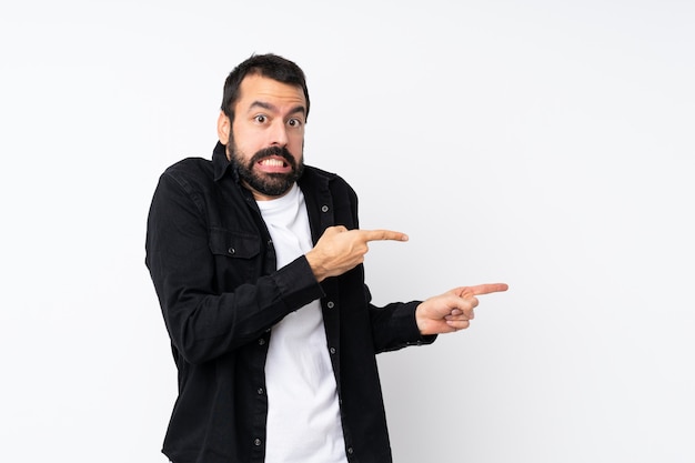 Young man with beard over isolated white frightened and pointing to the side