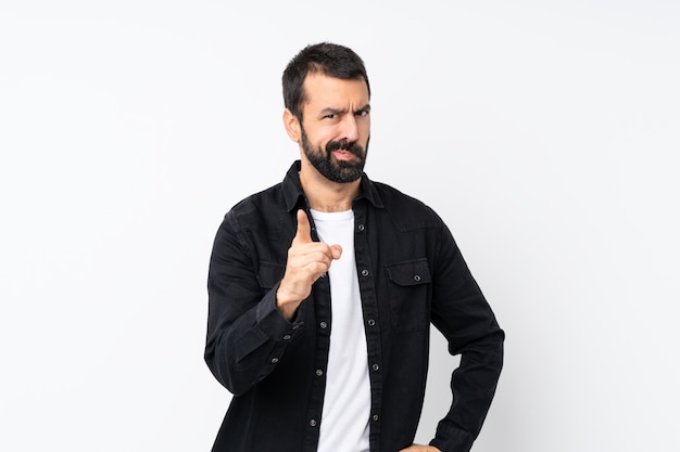 Young man with beard over isolated white wall frustrated and pointing to the front