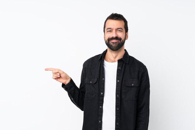 Young man with beard over isolated white wall pointing finger to the side