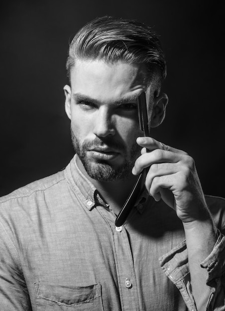 Young man with beard and mustache holding straight razor looking at camera professional barber with