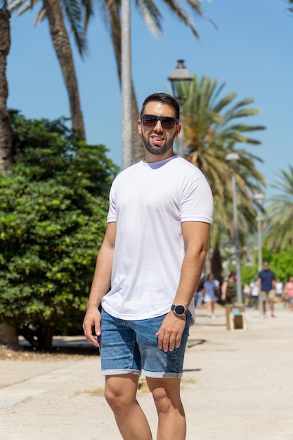 Young man with beard and sunglasses posing with palm trees in background