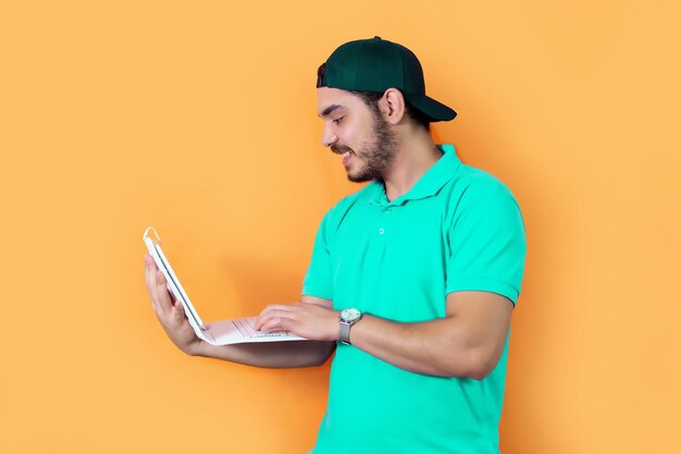 Young man with beard Tshirt and green cap using a tablet with keyboard on yellow background