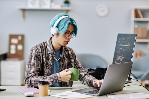 Young man with blue hair writing code