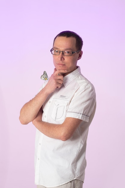 A young man with a butterfly on arm. Man in white clothes on a pale pink background