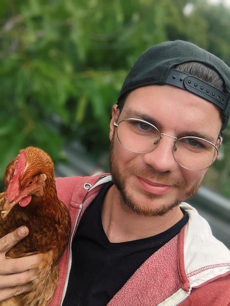 Photo young man with cappy has friendly chicken on his arm