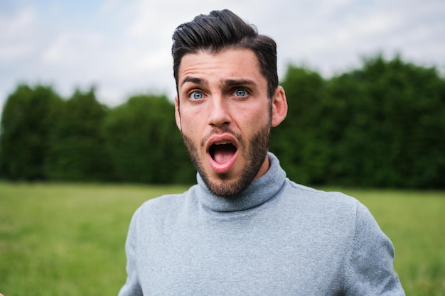 Young man with clear eyes with a face of huge surprise outdoors in the park