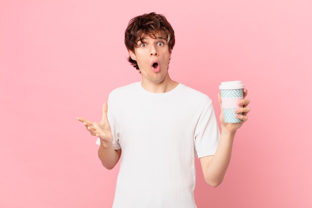 Young man with a coffee feeling extremely shocked and surprised