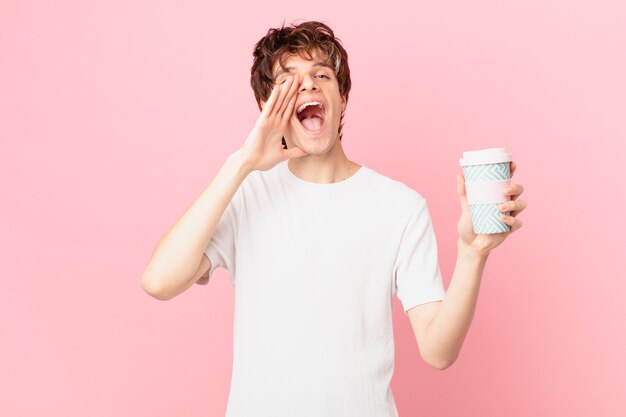 Young man with a coffee feeling happy,giving a big shout out with hands next to mouth