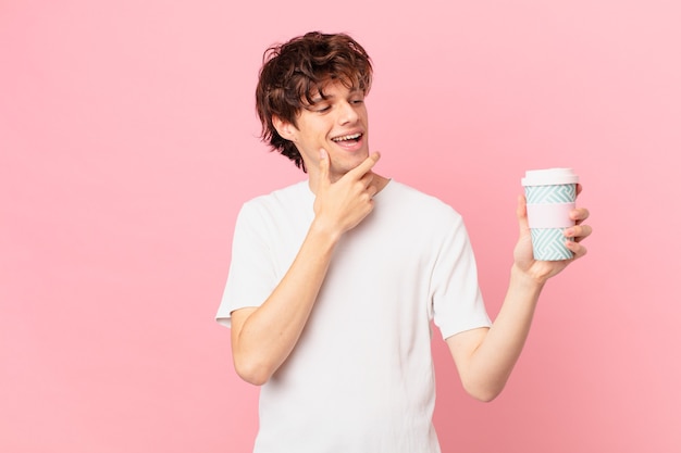 Young man with a coffee smiling with a happy, confident expression with hand on chin