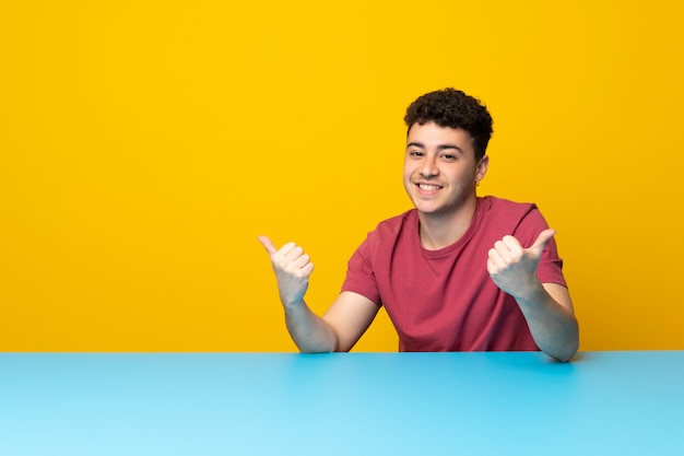 Young man with colorful wall and table with thumbs up gesture and smiling