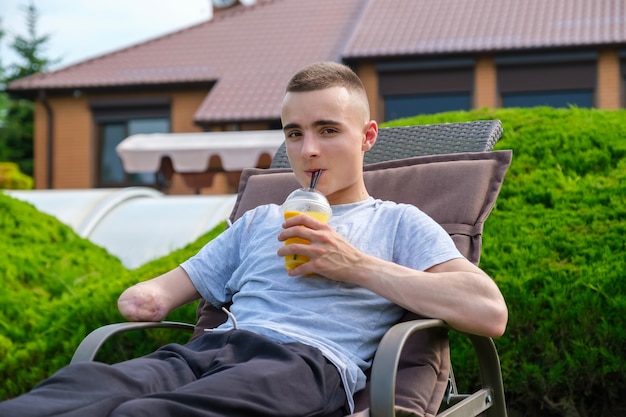 Young man with disability lies on a sun lounger and drinks cocktail