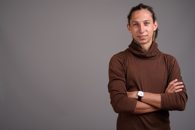 Young man with dreadlocks wearing brown shirt against gray backg