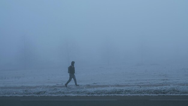 Young man with face mask walking alone on sidewalk in deep fog