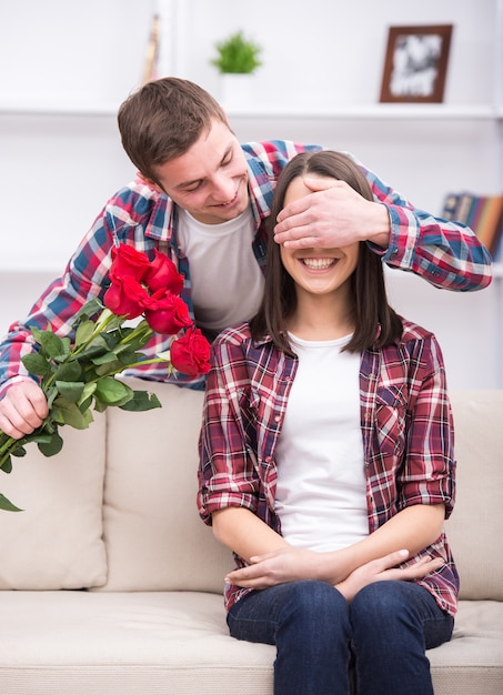 Young man with flowers is covering his girlfriend's eyes.