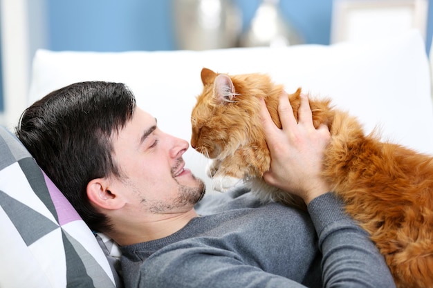 Young man with fluffy cat lying on a sofa