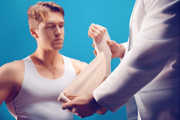 young man with hand injury in the doctors office The doctor makes a bandage to the patient