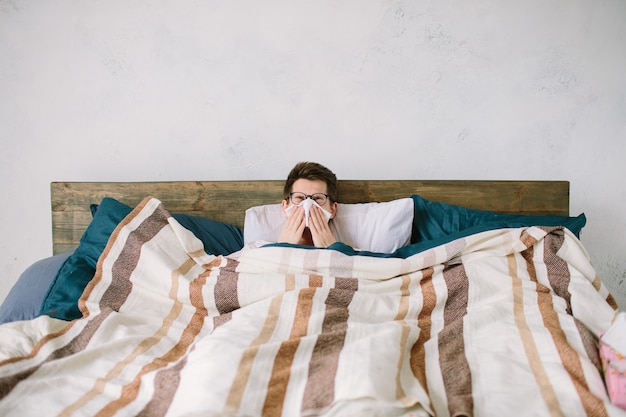 Young man with handkerchief. Sick guy on the bed has runny nose. man makes a cure for the common cold.