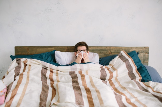 Young man with handkerchief. Sick guy on the bed has runny nose. man makes a cure for the common cold