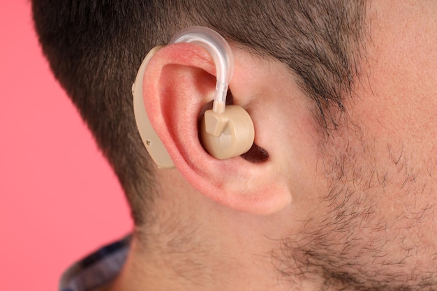 Young man with hearing aid on pink background