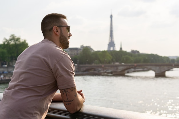 Young man with his back against a bridge in the foreground overlooking the Eiffel Tower and the Seine River