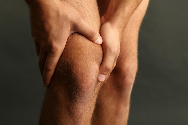 Young man with knee pain on dark background