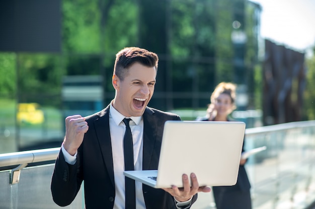 Young man with a laptop enthusiastically rejoicing