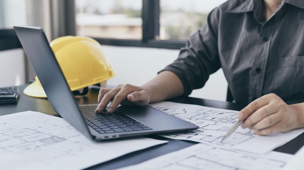 Young man with a laptop plotting a system of building structures in blueprints