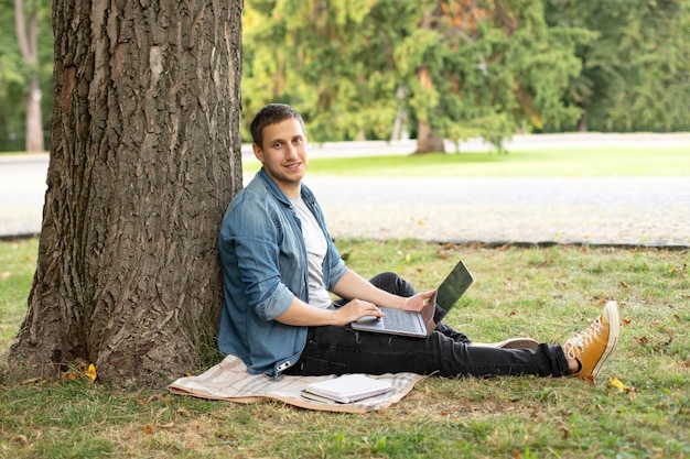 Young man with laptop rest in grass at university campus.