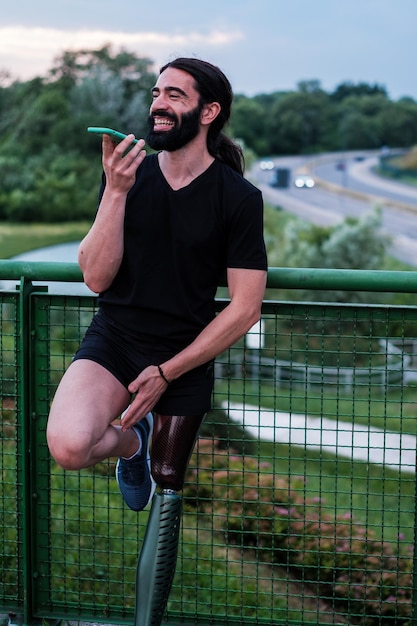 Young man with long beard hair talking on the smartphone outdoors Prosthesis