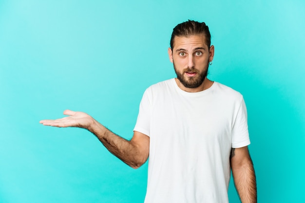 Young man with long hair look impressed holding copy space on palm.