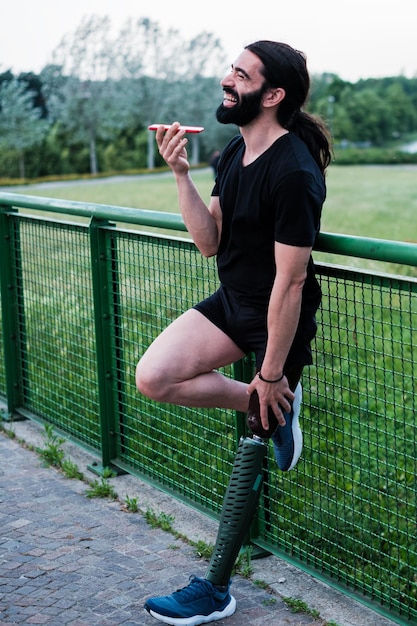 Young man with long hair and orthopedic leg talking on the mobile with his friends