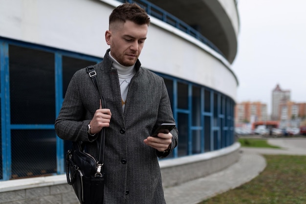 Young man with a mobile phone and a business bag on the background of a parking lot