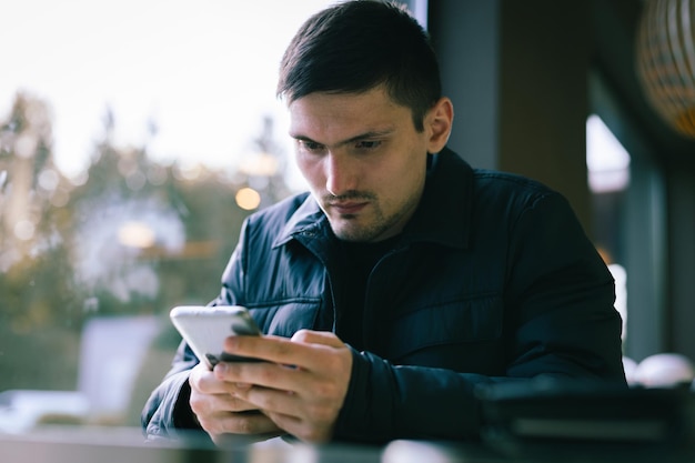 A young man with a phone in his hands is sitting in a diner