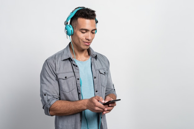 Young  man with pleasure listen to music in the earphones and looking at the phone's screen 