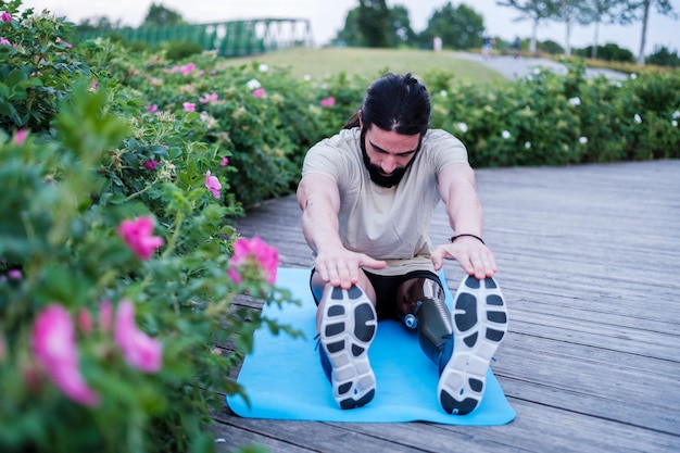 Young man with prosthetic leg doing stretching outdoors at sunset