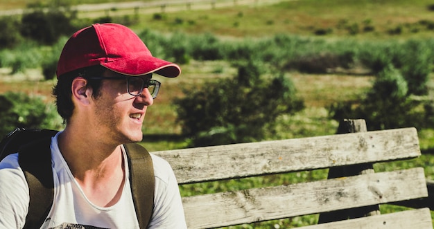 Young man with red cap sitting on a wooden bench