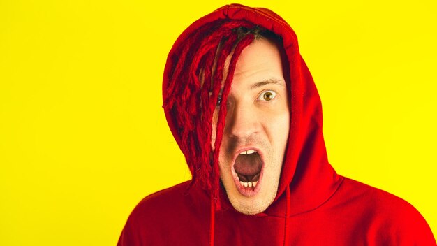 Young man with red dreadlocks in hood grimacing face Crazy guy aping