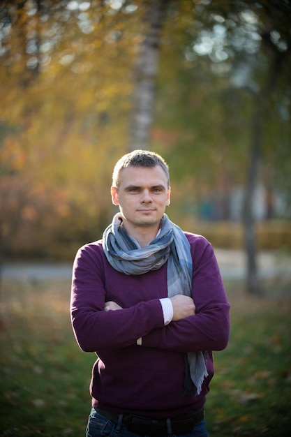 A young man with a serious look looks at the camera inthe autumn park