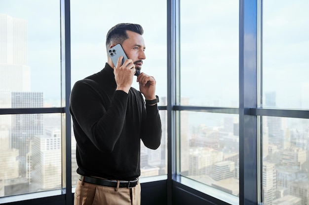 Young man with a smartphone standing near the window