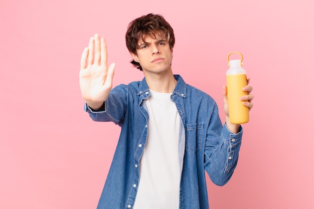 Young man with a smoothy looking serious showing open palm making stop gesture