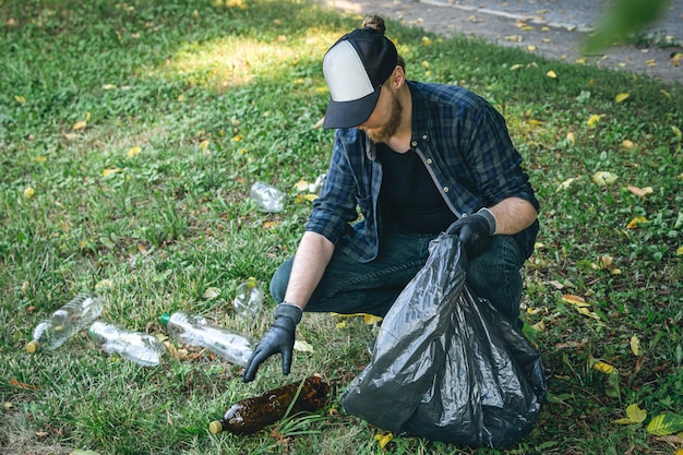 A young man with a trash bag in the forest cleans up plastic bottles