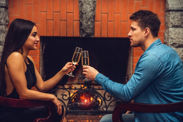 Young man and woman dating. THey sit in chairs and cheer with champaigne glasses. People look at each other. She smiles