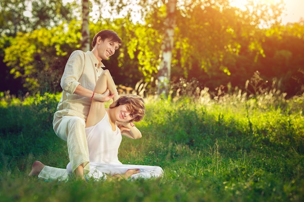 Young man and woman dressed in a white robe doing thai massage with yoga exercises sitting on the