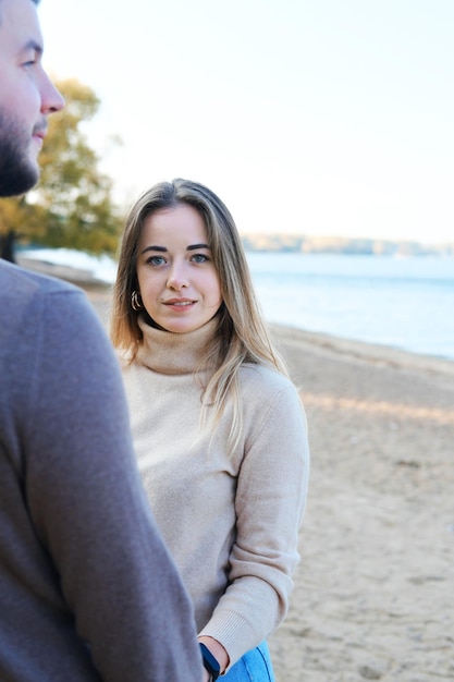 Young man and woman holding hands and posing on the beach The girl looks at the camera and smiles