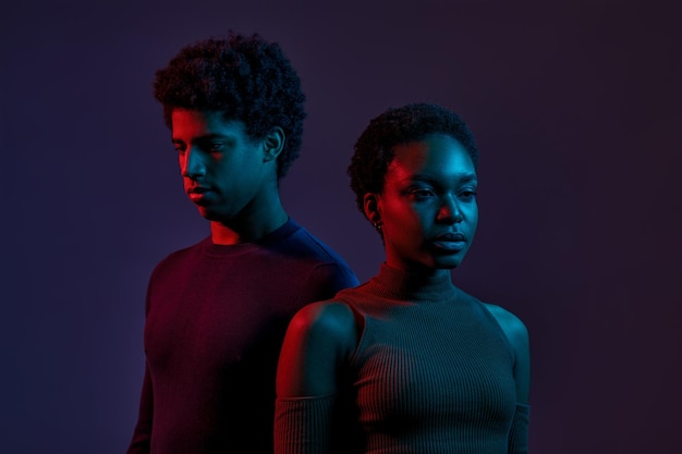 Young man and woman in neon light over dark background