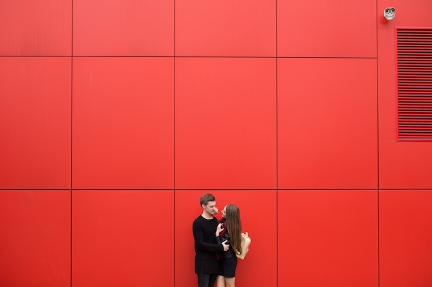 Young man and woman in passion, emotion, on the street with a backdrop of the red wall. Fashion