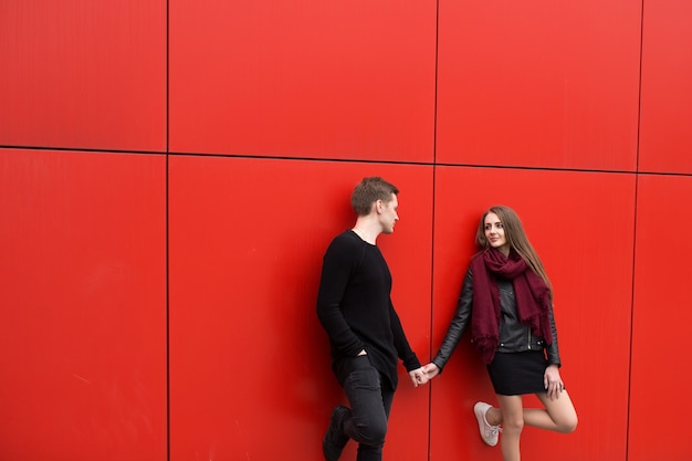 Young man and woman in passion, emotion, on the street with a backdrop of the red wall. Fashion